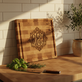 Personalized maple cutting board with monogram engraving propped against kitchen backsplash with fresh herbs and chef's knife