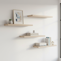 Three staggered white oak floating shelves on a minimalist home office wall with books, plant, and framed print