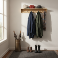 Shaker-style wall coat rack with two coats hanging from pegs, hats and scarves on pine shelf, soft morning entryway light