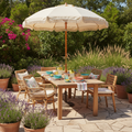 Grade-A teak outdoor dining table set for six on a summer patio with market umbrella, rattan chairs, and potted lavender