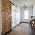 Knotty pine sliding barn door with Z-brace on black track in a modern farmhouse hallway, half-open revealing white bathroom